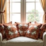 Set of burnt orange embroidered pillow covers arranged on white sofa near window, decorative cushion covers