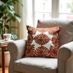 Close-up of burnt orange embroidered pillow cover showing detailed floral appliqué work on cotton fabric