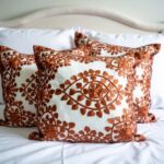Multiple burnt orange embroidered pillow covers on white bedding, handcrafted cotton cushions with medallion pattern