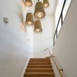 Handwoven straw lighting pendants illuminated in modern stairwell showcasing warm filtered light through weave