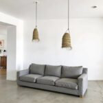 Handwoven straw lighting pendants above gray sofa in minimalist living room with natural texture
