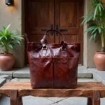 Burgundy brown leather tote bag on wooden bench displaying natural grain and contrast stitching