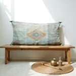 Handwoven cactus silk pillow 36 inch in sage green with diamond motif on wooden bench with natural decor