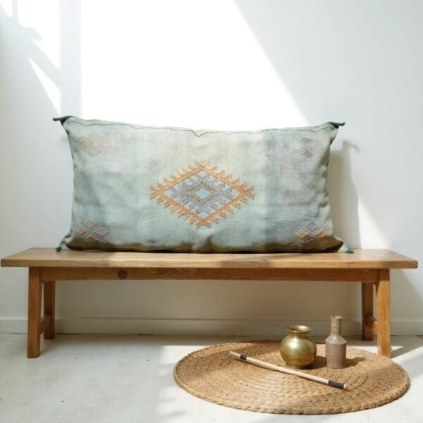 Handwoven cactus silk pillow 36 inch in sage green with diamond motif on wooden bench with natural decor