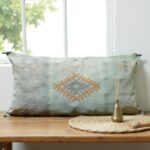 Handwoven cactus silk pillow 36 inch sage green with geometric pattern on wooden bench with candle holder