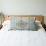 Handwoven cactus silk pillow 36 inch sage green diamond motif on white bedding with wooden headboard