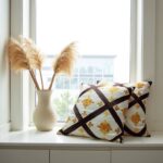 Woven diamond cushion covers on white windowsill with pampas grass, featuring golden medallion embroidery