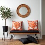 Embroidered cotton cushion pair styled on bench with round mirror, featuring orange damask pattern