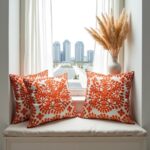 Embroidered cotton cushion covers with orange floral design on modern rattan chair near black window