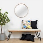 Embroidered pillow covers on minimalist bench with round mirror featuring vibrant floral motifs and scrollwork