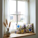 Multiple embroidered pillow covers on window sill showcasing handcrafted floral embroidery in bright colors