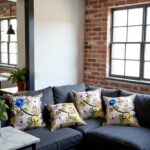 Embroidered pillow covers on gray sectional sofa in industrial loft displaying vibrant botanical garden motifs