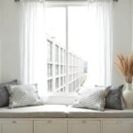 Gray embroidered cotton pillow covers with floral accents on window seat with drawers in bright room