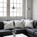 Set of three gray spiral embroidered cotton pillow covers arranged on dark leather sofa in industrial space