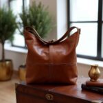 Close-up of cognac leather hobo handbag on wooden chest showing contrast stitching and grain texture
