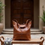 Handcrafted cognac leather hobo handbag on marble table with scenic Italian countryside view backdrop