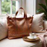 Cozy lifestyle shot of tan leather shopper bag on bed with coffee cup and soft pillows