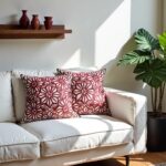 Red floral pillow covers on white sofa with sunlight, burgundy flower pattern cushions near green monstera plant