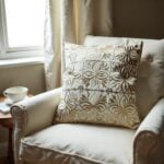 Two beige leather pillow covers with floral cutwork arranged on ivory sofa showing dimensional appliqué craftsmanship