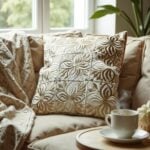 Beige leather pillow cover with floral cutwork on cream armchair next to coffee cup in cozy reading nook setting