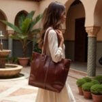 Elegant woman wearing white dress carrying cognac leather tote bag in Moroccan courtyard garden setting