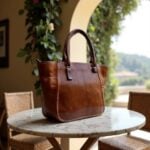 Brown leather tote bag with zipper on marble table, rustic Mediterranean background