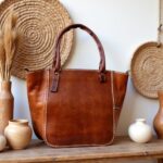 Brown leather tote bag with zipper displayed with woven baskets, bohemian home decor