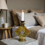 Sculptural green ceramic candle holder with lit white candle on marble surface creating ambient bedroom decor