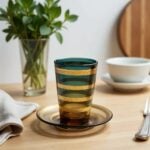 Close up of a forest green to amber gradient tea glass with gold painted bands and amber glass saucer