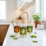 Three beautifully decorated oriental tea glasses displayed on a bright white quartz kitchen countertop, styled alongside scattered fresh mint leaves in a sunlit modern kitchen.
