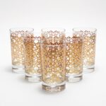 Set of six gold Moroccan tea glasses featuring a traditional geometric star pattern on clear glass, arranged against a seamless white background.