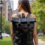 Woman carrying black leather backpack with expandable rolltop in outdoor urban setting