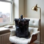 Handcrafted black leather backpack on modern chair showing adjustable padded straps