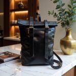 Black leather backpack rolltop design with brass hardware on luxury marble surface