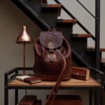 Brown woven leather backpack with basket-weave texture near window with laptop and coffee
