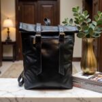 Full-grain black leather backpack with brass buckles on marble table in elegant interior