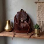 Close-up of woven leather backpack with basket-weave pattern on wooden shelf with brass accents