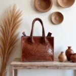 Artisan woven leather tote bag displayed with woven baskets, showcasing traditional basketweave leather craftsmanship