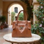 Cognac leather tote bag with turn-lock hardware displayed on marble table in arched courtyard