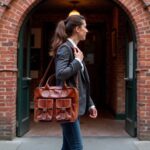 Full-grain leather laptop messenger bag worn crossbody by professional woman walking outdoors