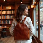 Woman in white blazer with woven leather backpack in library setting with bookshelves