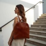 Woman on staircase wearing woven leather backpack in white sleeveless top and neutral outfit