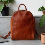 Handcrafted woven leather backpack in cognac brown on white marble countertop with plants