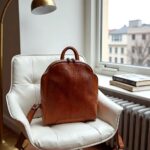Woven leather backpack on white modern chair by window with city view and natural light
