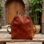 Woman in industrial loft wearing woven leather backpack with exposed brick and large windows