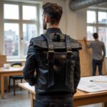 Professional wearing black leather backpack with brass buckles in contemporary office