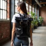 Woman wearing urban black leather backpack rolltop design in industrial loft space