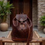 Full-grain woven leather backpack with basket-weave pattern on wooden deck entrance
