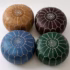 Four differently colored round pouffe ottoman seats—camel, espresso, blue, and emerald—arranged on a white studio backdrop.
