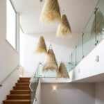 Multiple handwoven palm leaf pendant lights cascading down modern stairwell with glass railing